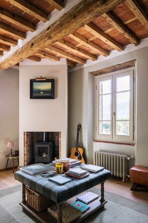 A cozy room with a fireplace, a guitar, a table with books, and a window with a view.