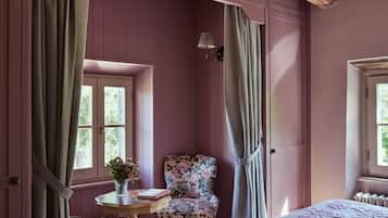 A bedroom with a wooden ceiling, a bed, a chair, a table with a vase, and a window.