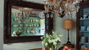 A dining area with a wooden table, chairs, a chandelier, and a mirror with a decorative frame.