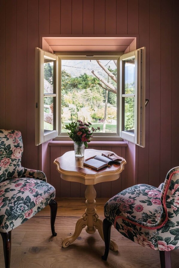 A room with a wooden bench, a small round table with a vase of flowers, and two chairs with floral upholstery.