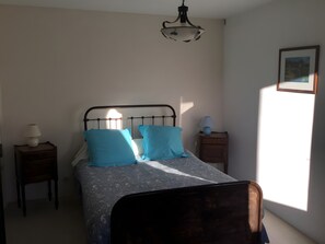 Ein Schlafzimmer mit einem Bett, einem Nachttisch mit Lampe, einer Kommode und einem Bild an der Wand.