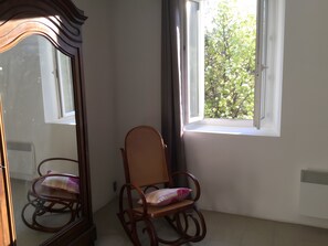 Ein Zimmer mit einem hölzernen Schaukelstuhl, einem großen Spiegel und einem Fenster mit Blick auf Bäume.