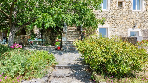 A stone building with a garden path leading to a door, surrounded by greenery and potted plants. - Cottage near Chauvet Cave and the Ardèche Gorges (Gras)