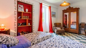 A room with two beds, a bookshelf, a chair, a mirror, and a window with red curtains. - Cottage near Chauvet Cave and the Ardèche Gorges (Gras)