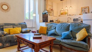 A living room with a sofa and a wooden coffee table, a kitchen area with a microwave and sink, and a large window providing natural light. - Cottage near Chauvet Cave and the Ardèche Gorges (Gras)