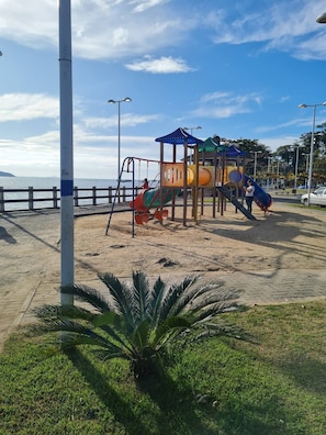 Ein Spielplatz mit Rutschen und Klettergerüsten, ein Sandstrand und eine Palme.