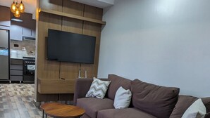 Un salon moderne avec un canapé marron, une petite table en bois et un téléviseur à écran plat fixé sur un mur recouvert de panneaux en bois.