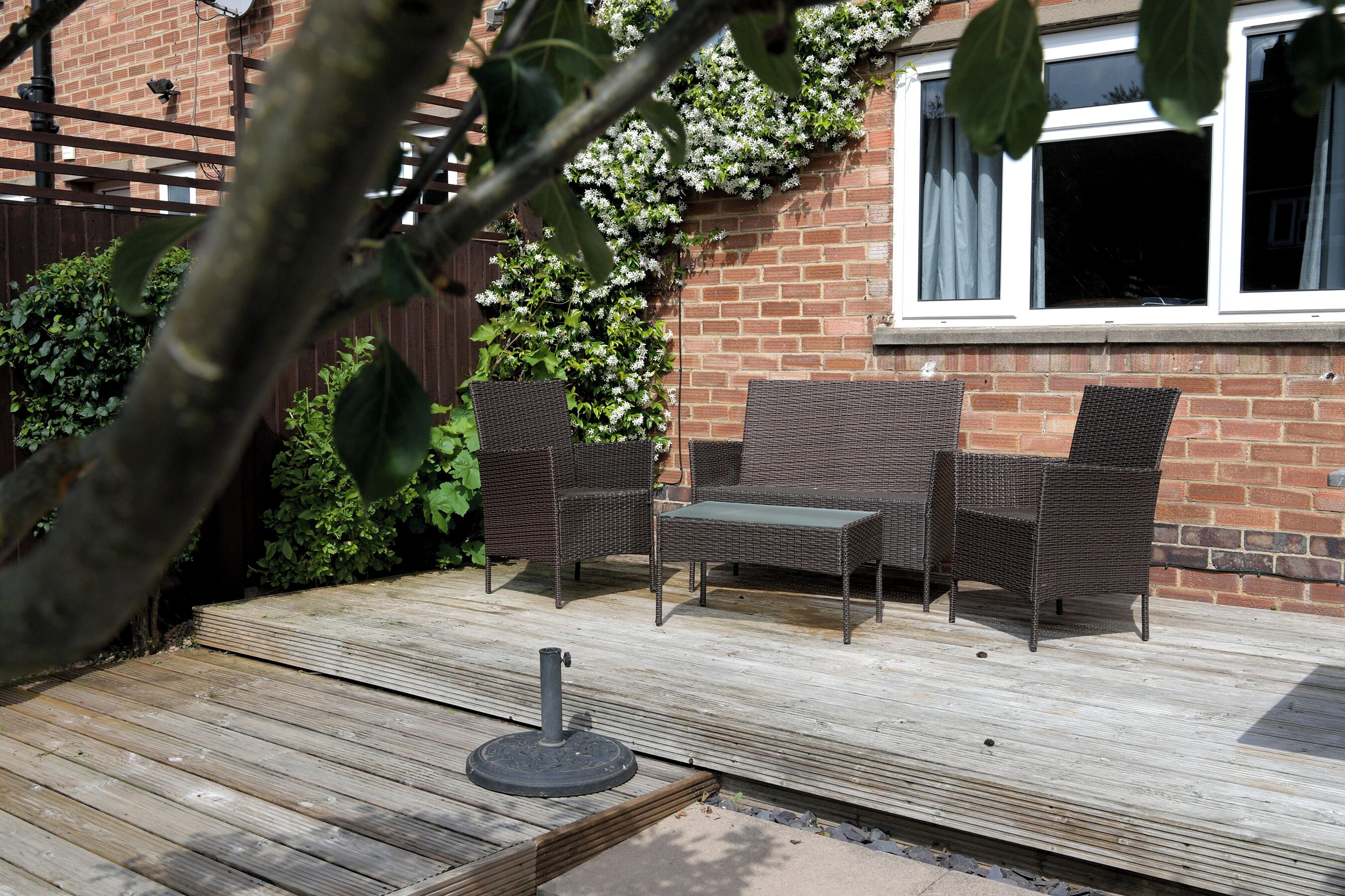 A patio with wicker furniture, a wooden deck, and a brick wall with a window.