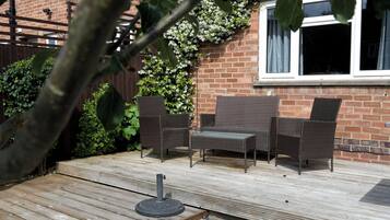 A patio with wicker furniture, a wooden deck, and a brick wall with a window.