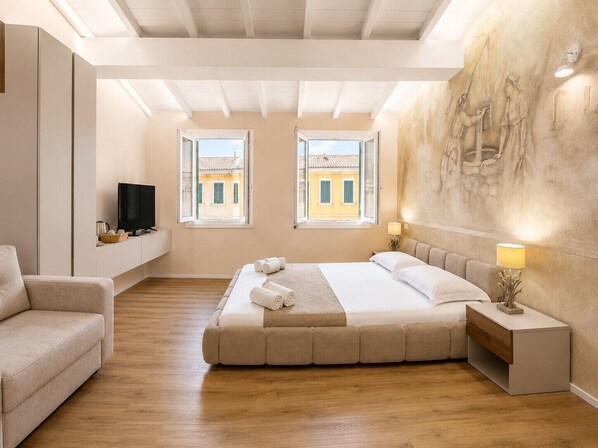 Un dormitorio con una cama grande, dos ventanas, un televisor, un sofá y una pared con un relieve escultórico.