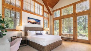 Ein Schlafzimmer mit einem großen Bett, Holzbalken, großen Fenstern, einer Bank und einem Nachttisch mit Lampe.