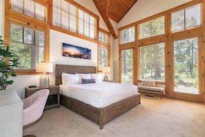 Ein Schlafzimmer mit einem großen Bett, Holzbalken, großen Fenstern, einer Bank und einem Nachttisch mit Lampe.