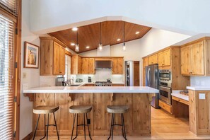 A modern kitchen with wooden cabinets, a central island with stools, and built-in appliances. - Old Greenwood Cabin 01 (Truckee)