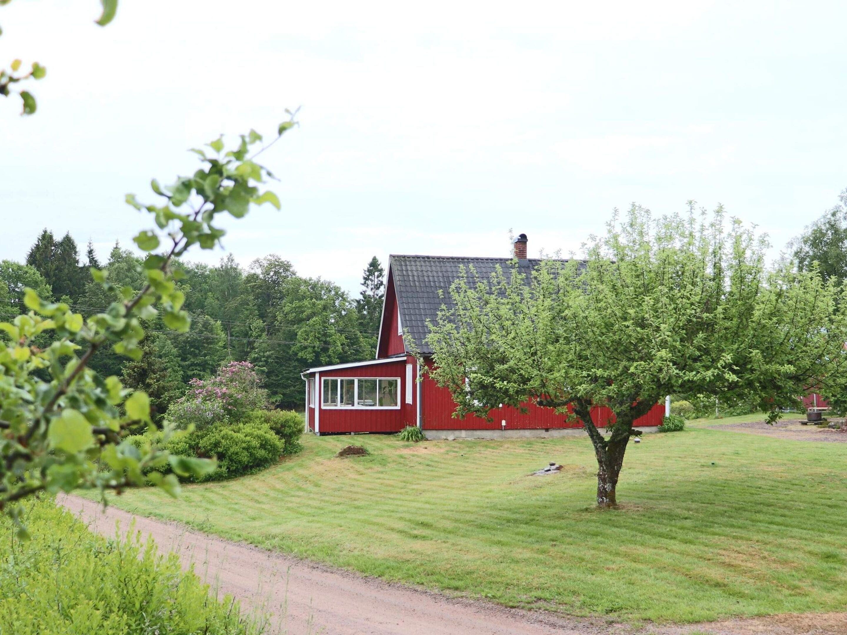 A red house with a sloped roof, surrounded by a well-maintained lawn and trees.
