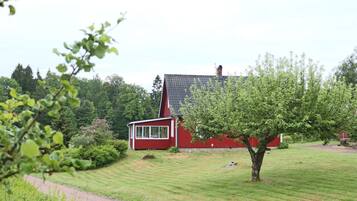 A red house with a sloped roof, surrounded by a well-maintained lawn and trees.