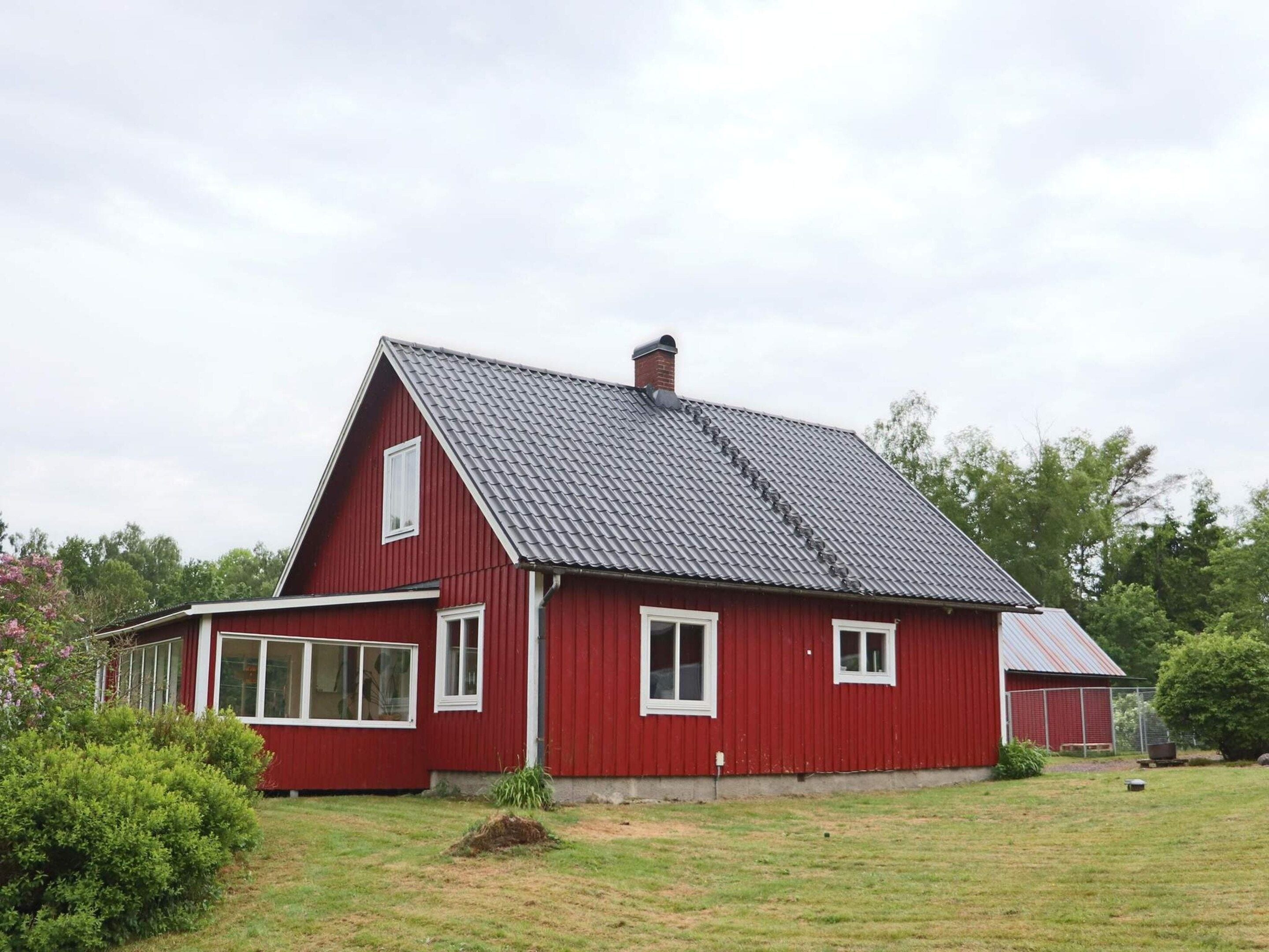 Ein rotes Bauernhaus mit geneigtem Dach, weißen Fenstern und einem grünen Rasen.