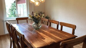 Un tavolo da pranzo con un vaso di fiori, sedie di legno, un lampadario e una finestra con vista sugli alberi.