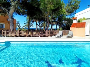 Une piscine aux eaux cristallines, des chaises longues, une clĂŽture en bois et des arbres en arriĂšre-plan.