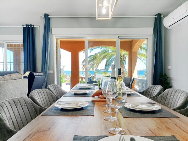 Un espace repas avec une longue table, des chaises et une vue sur la mer.