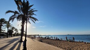 Una playa con un paseo marítimo empedrado, palmeras y gente disfrutando del agua.