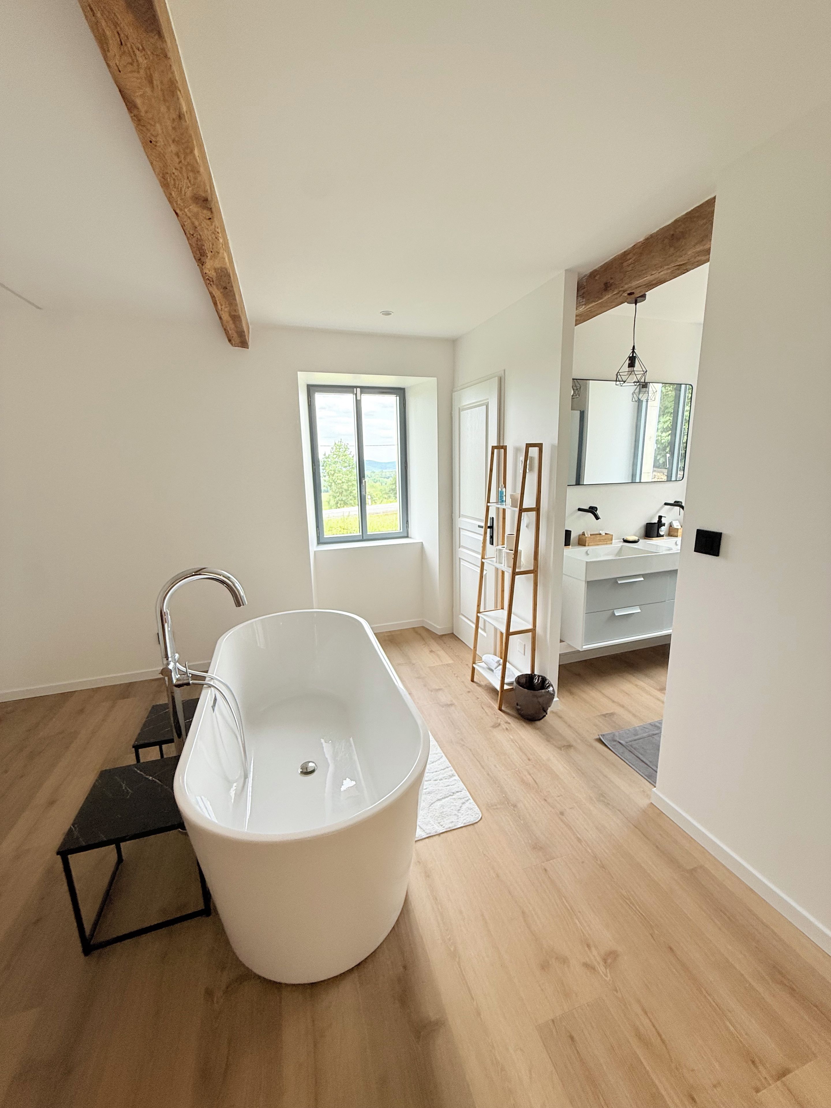Une salle de bain moderne avec une baignoire sur pieds, un plancher en bois, une grande fenêtre et un meuble-lavabo avec un miroir.