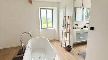 Une salle de bain moderne avec une baignoire sur pieds, un plancher en bois, une grande fenêtre et un meuble-lavabo avec un miroir.