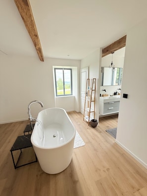 Ein modernes Badezimmer mit freistehender Badewanne, Holzboden, einem großen Fenster und einem Schminktisch mit Spiegel.