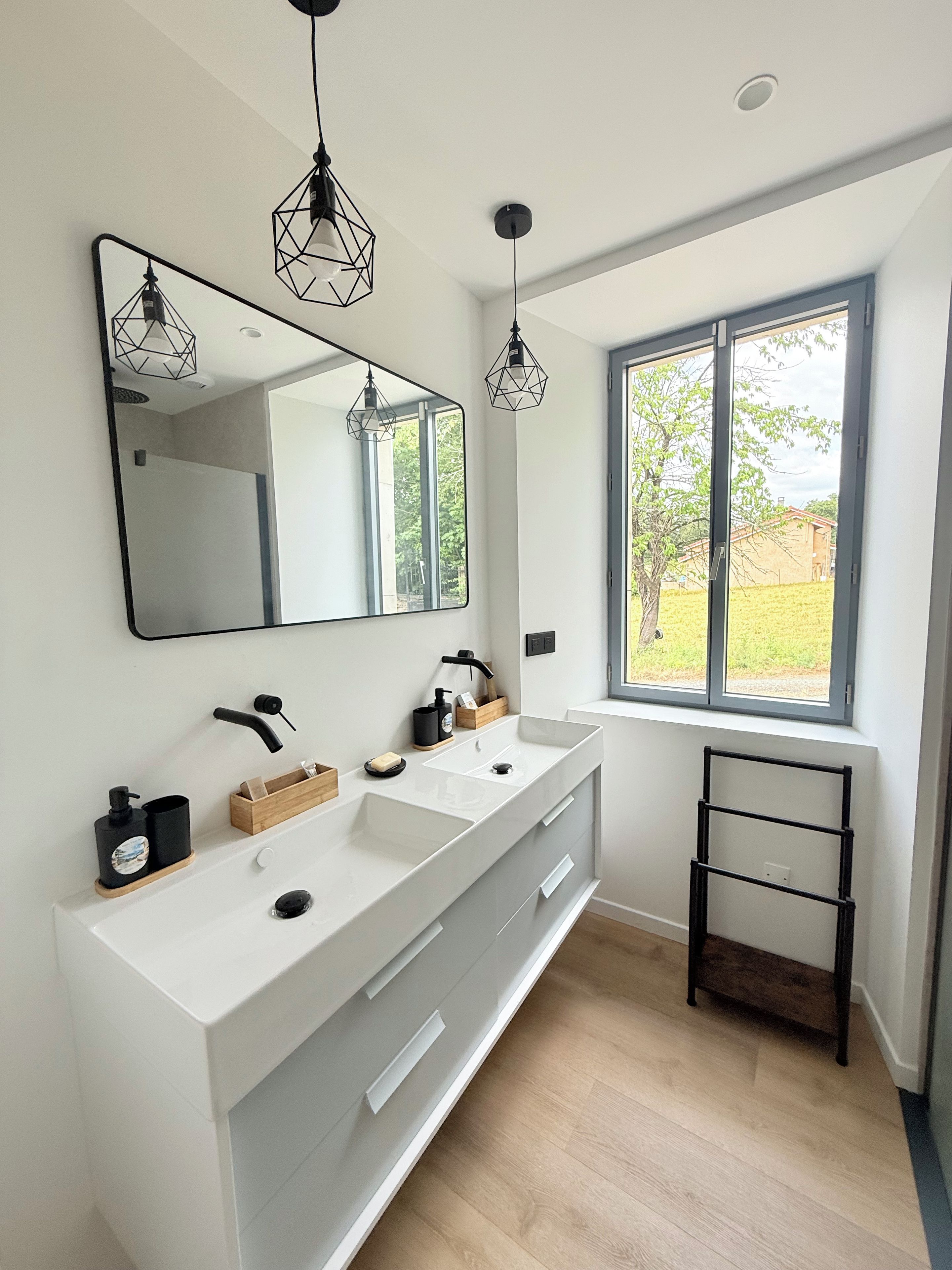 Een moderne badkamer met een grote spiegel, twee wastafels en een raam met uitzicht op groen.