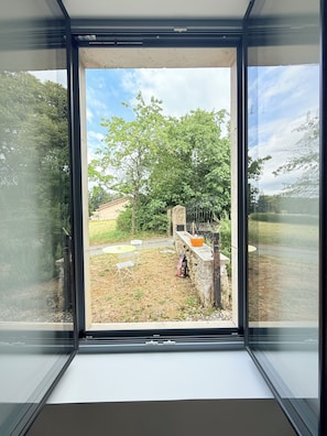 Ein Fenster mit Blick auf eine Wiese, eine Steinmauer und einen Baum.