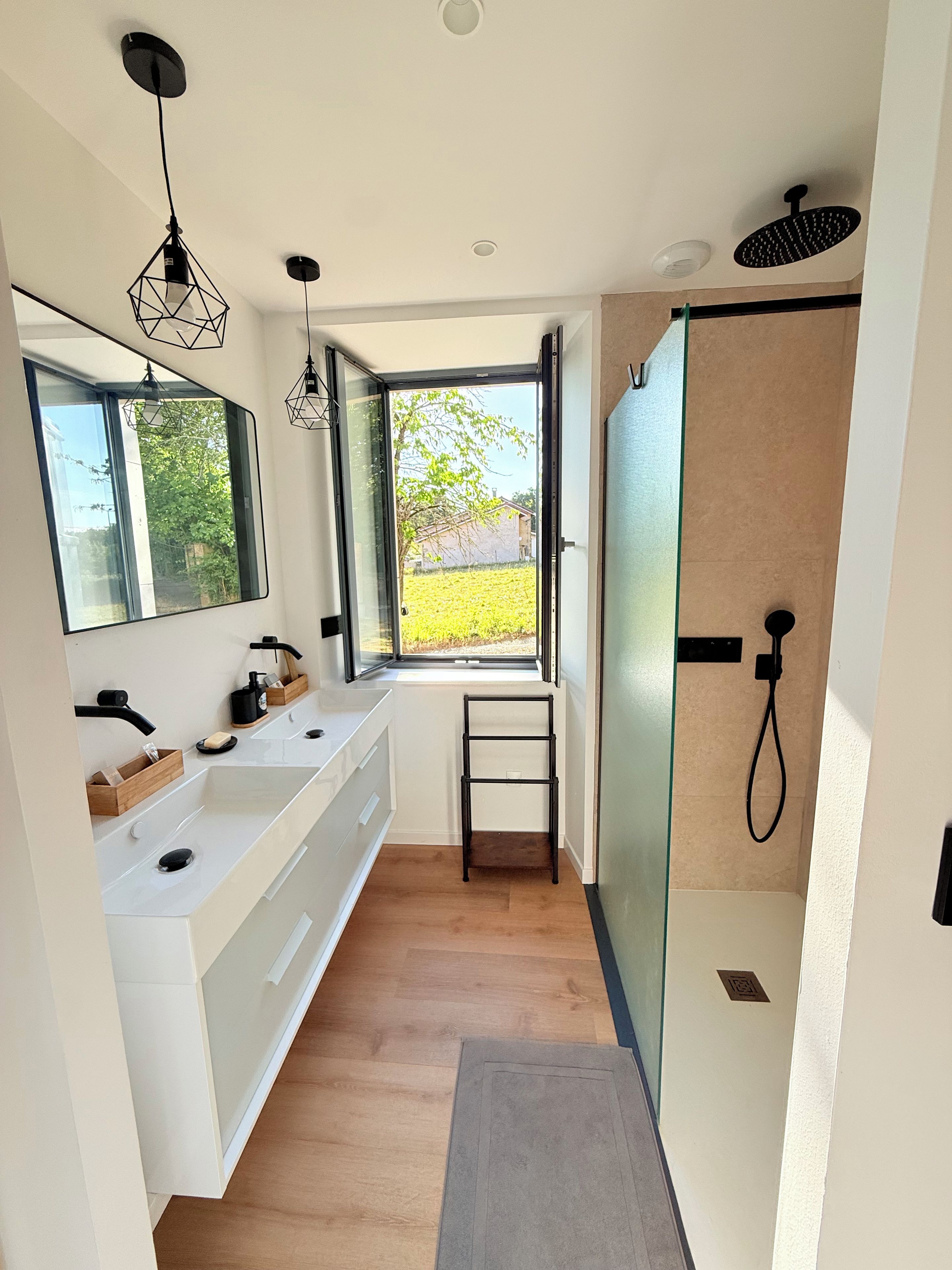 Een moderne badkamer met een groot raam, dubbele wastafels en een douchegedeelte.