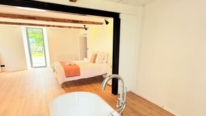 A modern bathroom with a freestanding bathtub, wooden flooring, and a visible bedroom in the background. - Suite - Îlot bath -Pyrenees view- Private entrance (Figarol)