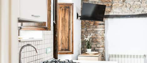 A modern kitchen with a gas stove, stainless steel sink, wooden cabinets, and a stone wall.