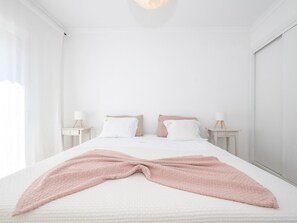 A minimalist bedroom with a bed, two bedside tables, and a window. - Rivara Rooftop Apartamento T3 de luxo (Cabanas de Tavira)
