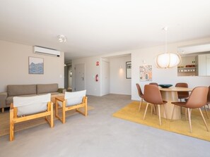 A modern living room with a sofa, a dining table with chairs, a hanging light fixture, and a fire extinguisher on the wall. - Rivara Rooftop Apartamento T3 de luxo (Cabanas de Tavira)