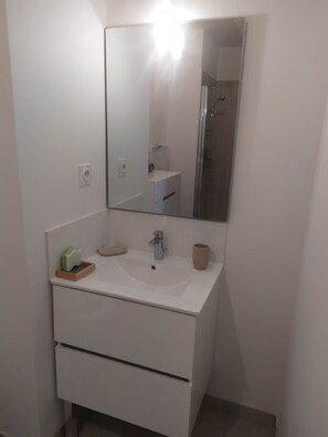 A bathroom with a white sink, a mirror, a shower, and a towel rack. - Recent 25m2 studio with parking space (Aytré)