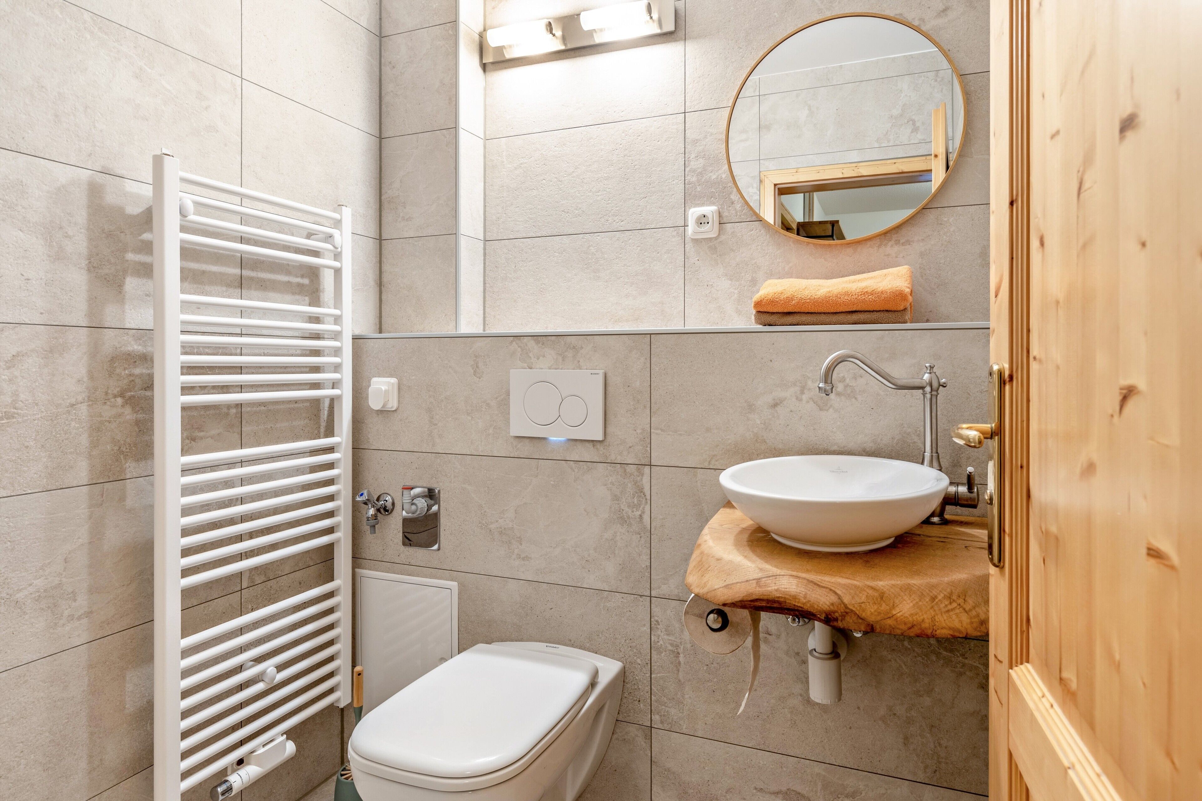 Ein Badezimmer mit einer weißen Toilette, einem Handtuchhalter, einem Waschbecken mit Holzplatte, einem Spiegel und einem Handtuch an der Wand.