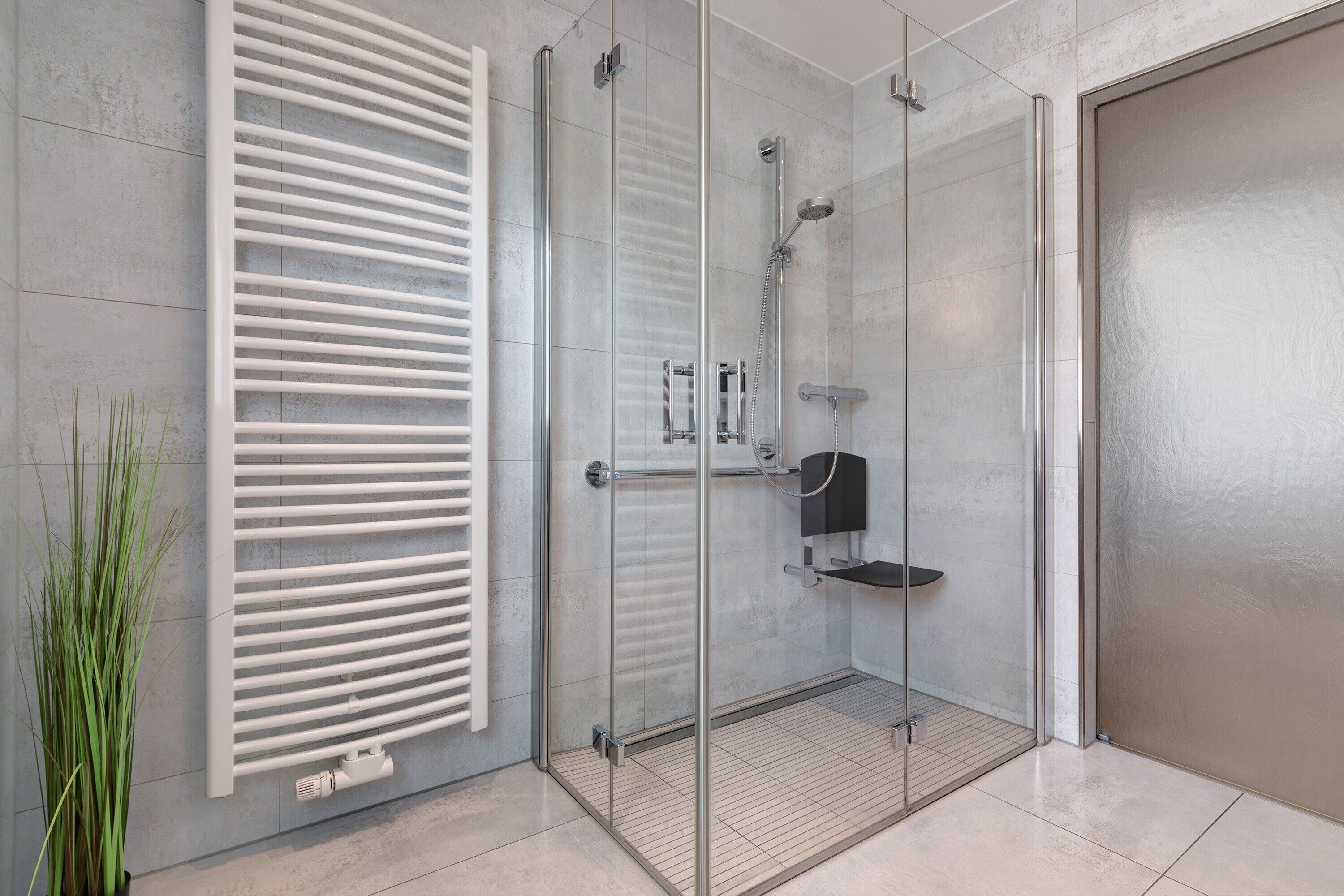 Un baño moderno con cabina de ducha de vidrio, toallero blanco y un pequeño estante con artículos de aseo.