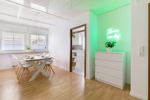 Un espace repas moderne avec une table et des chaises en bois, un panneau néon et un meuble blanc.
