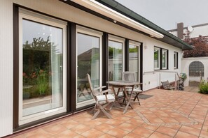 Une terrasse avec une table et des chaises, de grandes portes-fenêtres coulissantes et un mur extérieur blanc.