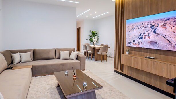 Un soggiorno moderno con un divano componibile, un tavolino, una TV a schermo piatto montata su una parete di legno e un'area pranzo con sedie e tavolo.