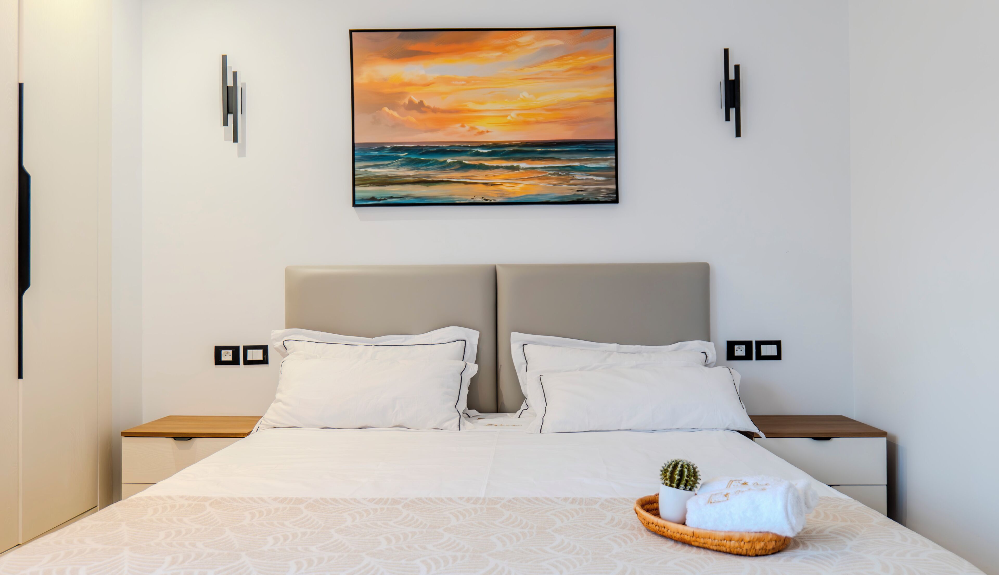 Une chambre d’hôtel avec un grand lit, deux tables de chevet, un tableau accroché au mur et un petit cactus posé sur le lit.