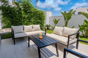 An outdoor seating area with a black table and two sofas, surrounded by greenery and a white building. - Djerba Appart 2 Royal (Houmet souk Djerba)