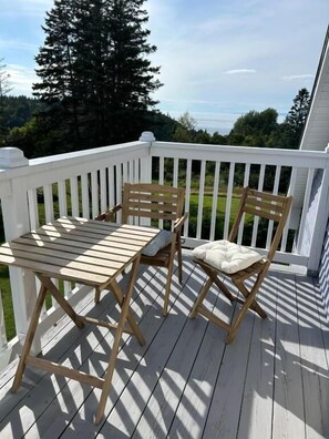 A wooden deck with a white railing, two wooden chairs, and a table. - Tides Inn Guest Suites (Halls Harbour)