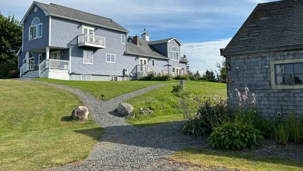 A two-story house with a front porch, a driveway, and a small garden area. - Tides Inn Guest Suites (Halls Harbour)