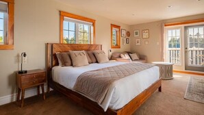 A bedroom with a large bed, a nightstand, a dresser, and a window with a view. - Tides Inn Guest Suites (Halls Harbour)