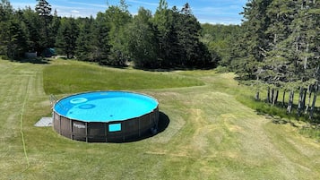 Une piscine ronde, entourée d’une pelouse verdoyante, avec des arbres en arrière-plan.
