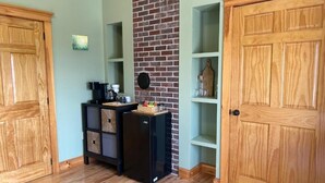 A room with wooden flooring, a black refrigerator, a coffee maker, and a brick wall. - Tides Inn Guest Suites (Halls Harbour)