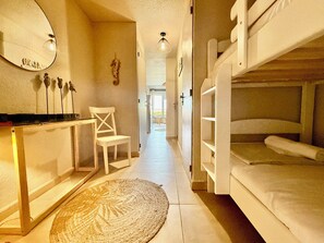 A compact room with bunk beds, a small desk, a chair, a mirror, and a woven rug.