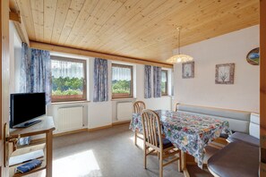 A room with a wooden ceiling, a television on a stand, a dining table with chairs, and windows with curtains. - Apartment 'Bel Udëi' with Mountain View, Shared Pool and Wi-Fi (San Martino In Badia)