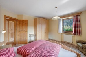 A room with a bed, a window with curtains, a radiator, and a wooden door. - Apartment 'Bel Udëi' with Mountain View, Shared Pool and Wi-Fi (San Martino In Badia)